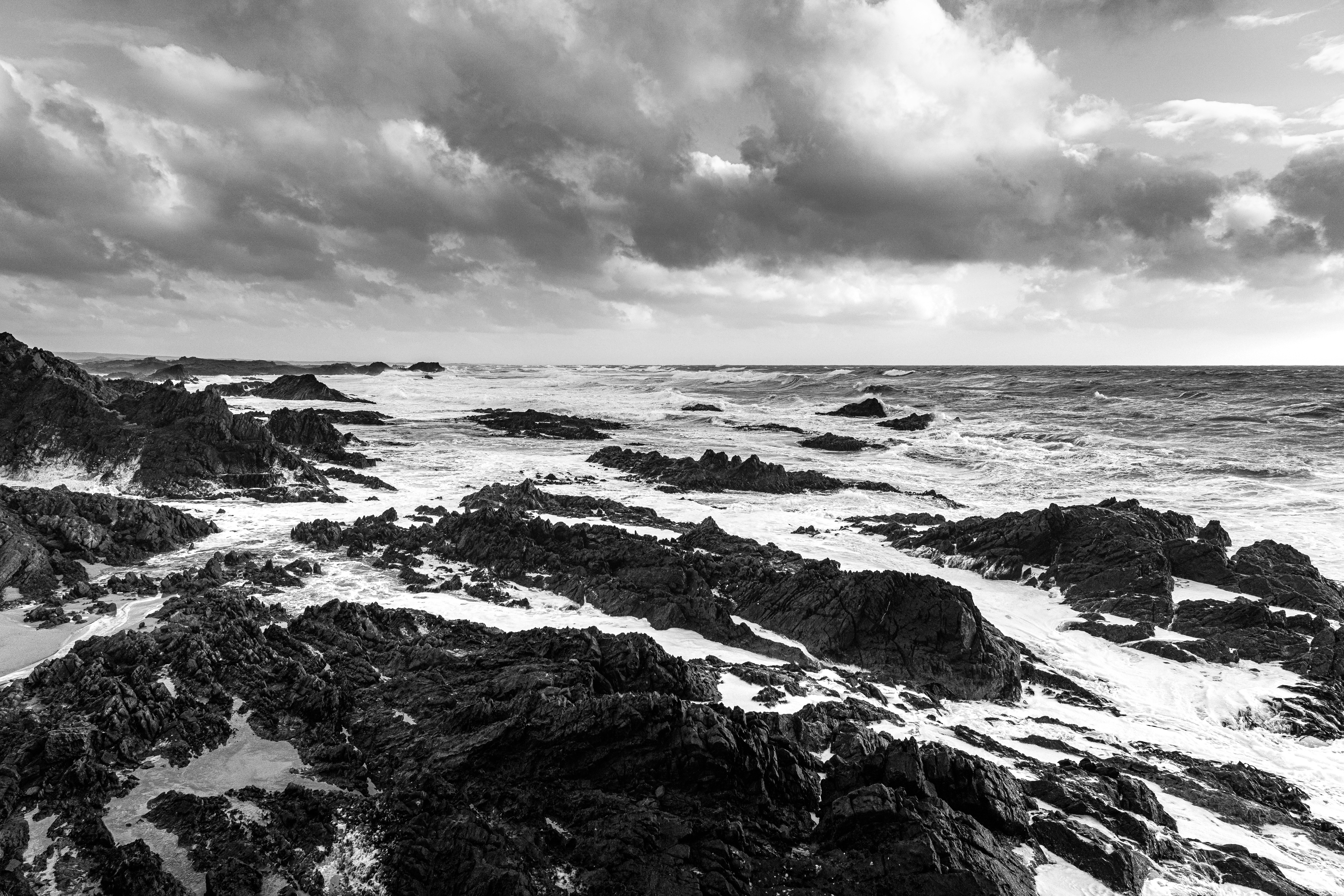 grayscale photo of rocky shore under cloudy sky